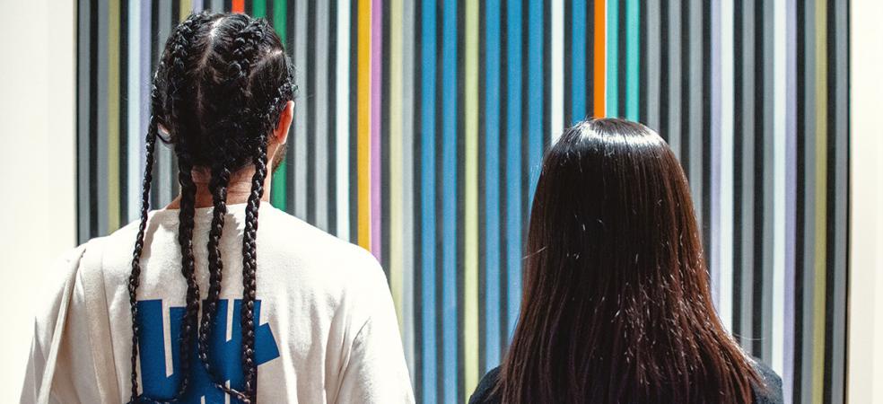 Photograph of two people standing looking at a striped painting