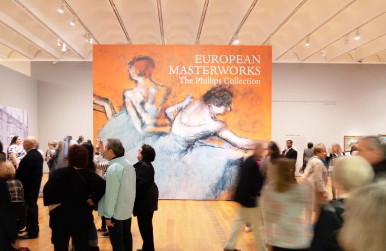 Photograph of a gallery with a lot of people mingling and a very large reproduction of Degas's Dancers at the Barre painting