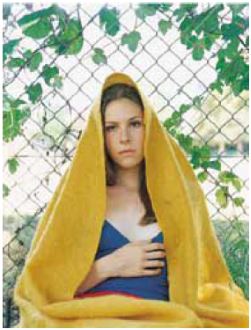 Woman with blue shirt and yellow quilt draped over her head and body