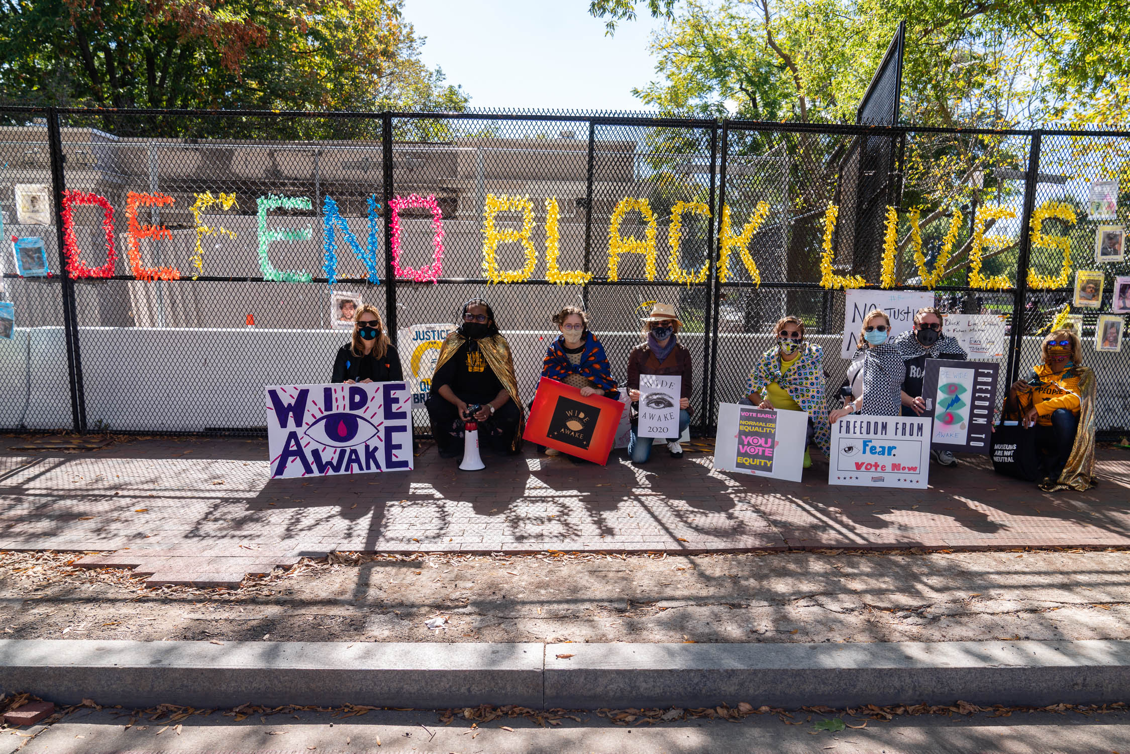 Photograph of people by a fence that says Defend Black Lives