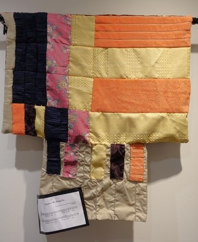 Orange, yellow, pink, and black quilt in a piano shape.