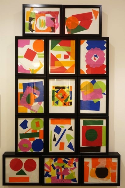 14 framed, colorful collages displayed closely together on the wall.