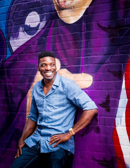 Photograph of Anieka Udofia smiling and standing against a purple wall