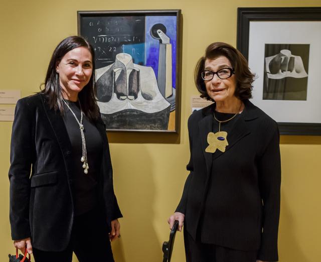 Photograph of two women standing with two artworks on the wall, smiling at the camera