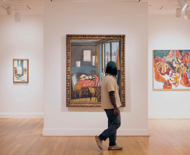 Man walking in front of three paintings in an art museum