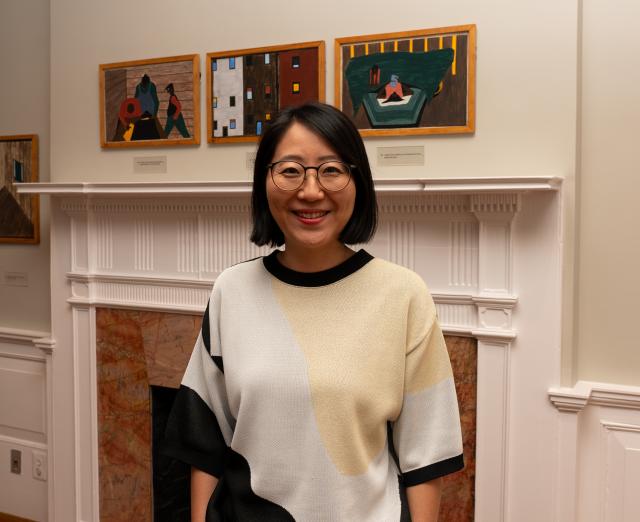 A woman standing in front of a fireplace with paintings hanging above the mantle