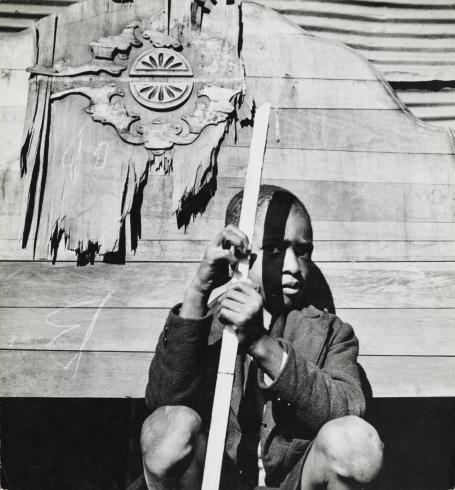 black and white photograph of child holding stick in front of building