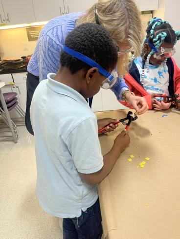 Phillips educator helping student cut mosaic tiles in art workshop.