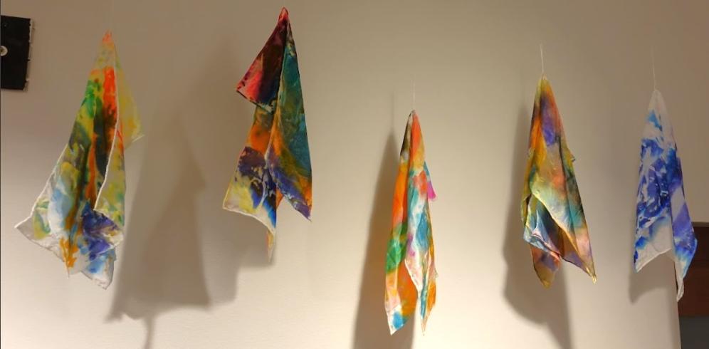 5 silk scarves dyed in various colors displayed from the ceiling.