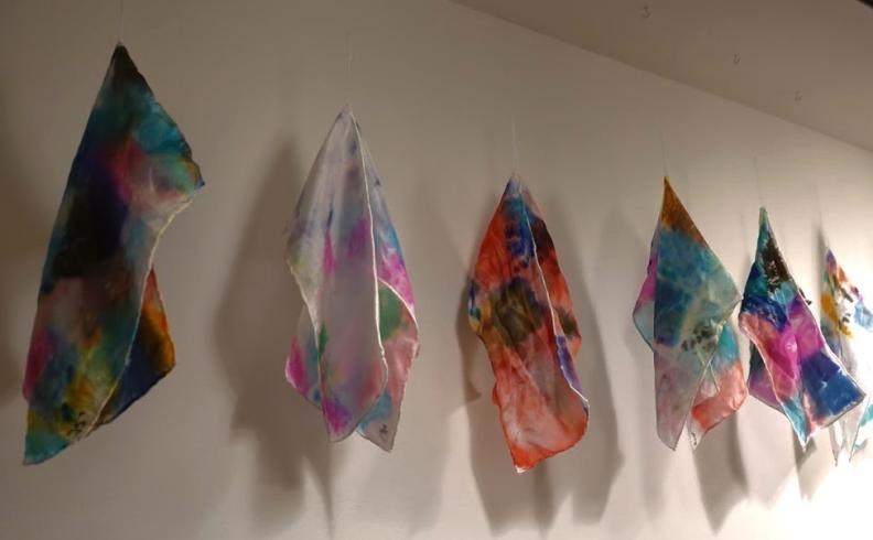 6 silk scarves dyed in various colors displayed from the ceiling.