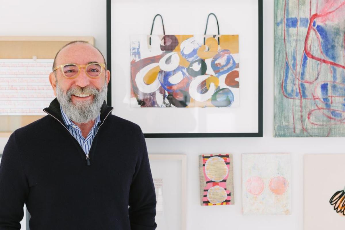 Photograph of Dani Levinas smiling in front of a wall of artwork
